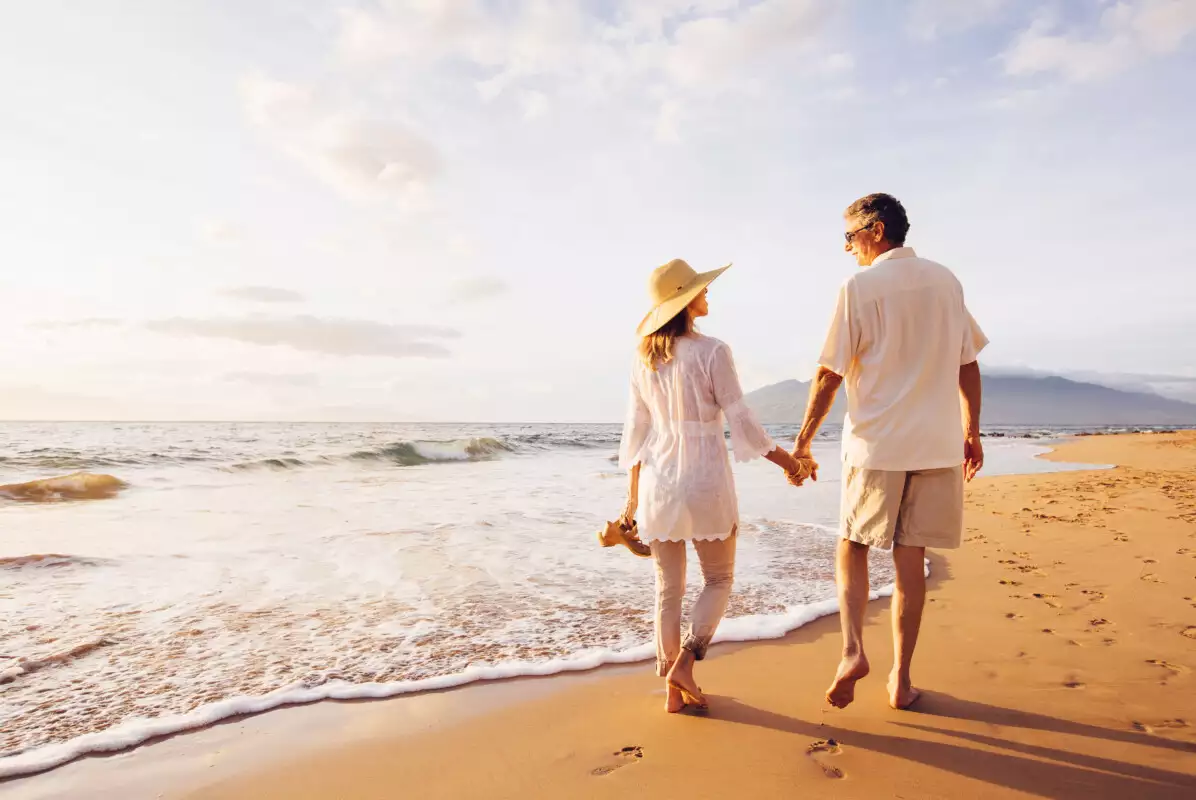 Older couple walking the beach together that is sunny and bright